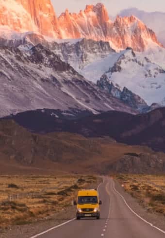 Κίτρινο camper van σε ανοιχτό δρόμο κάτω από τον χιονισμένο ορεινό όγκο Fitz Roy στην Παταγονία